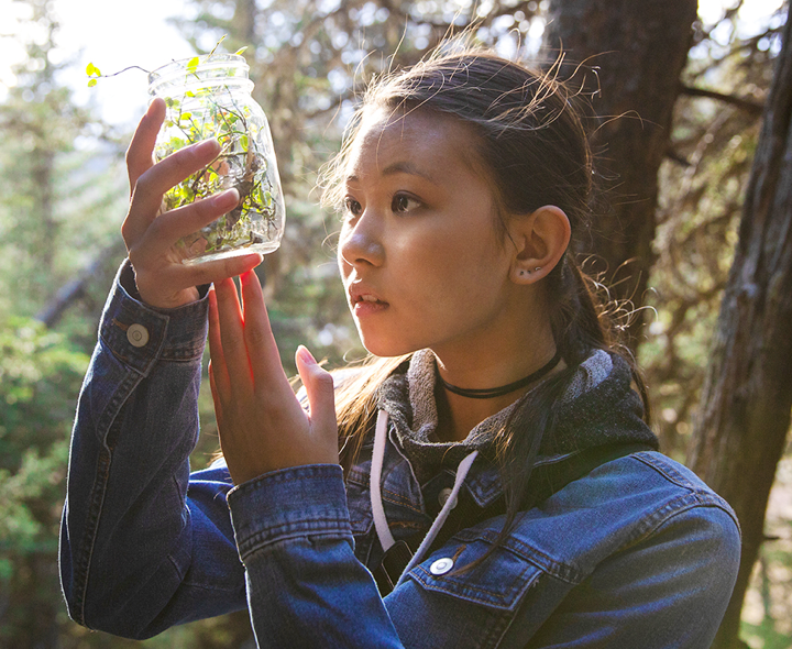 Girl looking at plants in a mason jar.